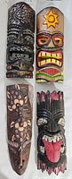 Top-down photo of four tiki style wooden wall masks in various colors and designs.
