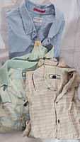 Three folded Tommy Bahama shirts showing different colors and patterns: light blue, cream with stripes, and tropical floral print.