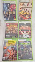 Six Xbox 360 game cases arranged in two rows of three. Includes titles L.A. Noire, Full Auto, LEGO Indiana Jones, Don King's Prizefighter, Deadliest Catch Sea of Chaos, and Teenage Mutant Ninja Turtles.