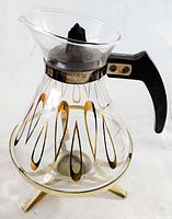 Glass carafe with decorative gold and black teardrop pattern and black handle shown from side