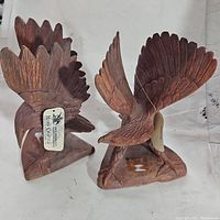 Pair of hand carved wooden eagle sculptures side by side, showing detailed feathers and base