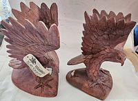 Pair of hand carved wooden eagles with tags visible, showing size and detailing of feathers and wings from front and side angles.