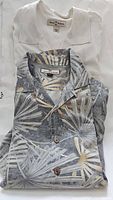 Image of two folded Tommy Bahama button-down shirts, one solid white and one with gray and beige palm leaf pattern.