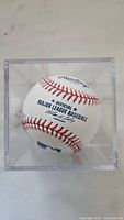 Official Major League Baseball with visible branding and red stitching inside clear display case.