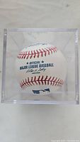 Official Major League Baseball ball with MLB branding visible inside a clear plastic display case.