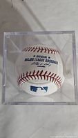 Top view of official Major League Baseball inside a transparent acrylic display case showing MLB logo and official signatures printed on ball.