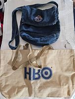 Photo showing the full view of both bags: the blue denim crossbody Gitano bag on top and the beige HBO tote bag below.