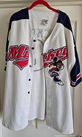 Front view of a white baseball-style jersey with navy sleeves, red 'Mickey' script across the chest and an embroidered Mickey Mouse swinging a bat.