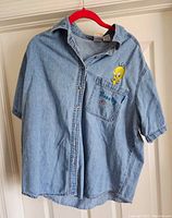 Full view of the light blue vintage denim short-sleeve shirt with button snaps and collar, hanging on a red hanger.