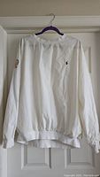 Rear view of white Polo Ralph Lauren golf pullover on hanger showing embroidered logo on chest and ribbed hem and cuffs.
