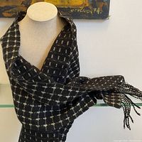 Full view of black scarf with white linear pattern displayed on a mannequin, showing fringed ends.