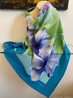Silk scarf displayed on a stand showing the large blue and green floral and leafy pattern and turquoise border.