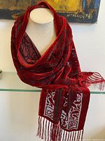 Scarf draped on a display bust showing red velvet material with floral pattern and hand tied fringes on ends.