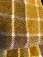 Close-up image of wool fabric showing mustard, brown, and cream plaid pattern and texture of wool fibers.
