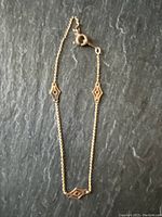 Full view of delicate gold bracelet on dark slate background showing entire length and clasp.