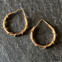Pair of gold hoop earrings laid flat on a dark surface, clearly showing the braided wire design wrapped around the tubular hoop.