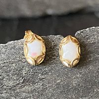 Photo of both earrings showing the opal stones in yellow gold scalloped bezels laid on a textured stone surface.