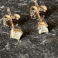Close-up front view of a pair of 10K gold stud earrings with small claws holding clear stones.