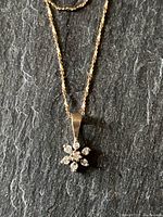 Close-up of flower-shaped diamond cluster pendant on rope chain against slate background