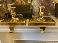 Pair of polished brass weighted stocking hangers with integrated candle holders on mantle shelf.