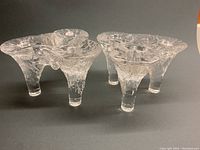 Pair of clear textured glass candle holders with three legs each, showing icicle-like frosty texture and organic shapes from front angle.