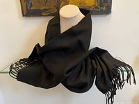 Black scarf displayed on a mannequin, showing the soft texture and fringed ends.