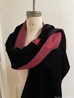 Black velvet shoulder wrap draped on mannequin showcasing velvet side with burgundy lining visible.