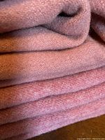 Close-up image showing folded wool blankets in coral shades with visible texture and soft fibers.