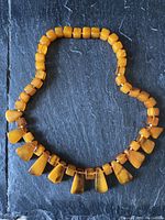 Full view of the amber bead necklace arranged in a circle on a dark textured surface, showing the graduated bead sizes and coloration.