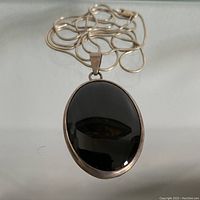 Full view of sterling silver snake chain with black onyx oval pendant laid flat