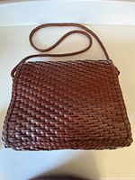 Front view of cinnamon brown leather shoulder bag with woven basket pattern and braided edges, with attached braided strap.