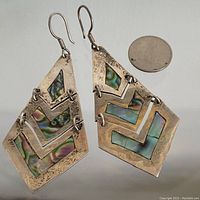 Pair of sterling silver earrings with abalone shell inlays and hinged triangular design shown near a quarter for scale.