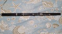 Full view of the antique wood piccolo flute showing its length, copper lining near embouchure, and black finish.