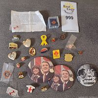 Full assortment of buttons and pins laid out on a fabric surface, including Canadian and political themed items