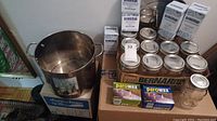 Photo of a large stainless steel stock pot sitting on a box, next to several Bernardin mason jars with lids, five unopened boxes of Bernardin canning jars and two boxes of Parowax paraffin wax.
