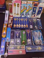 Overview of multiple boxed and loose collector spoons arranged on a surface, showing variety of designs and origins