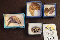 Four pieces of copper jewelry arranged in original boxes: copper feather brooch, feather earrings, theater masks pin, and an additional feather brooch.