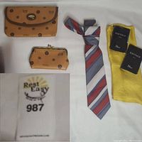 Photo of two Classic brand tan leather wallets with monogram pattern, Oscar De La Renta striped tie, and two Dior Sauvage Parfum tester bottles on yellow cloth bags