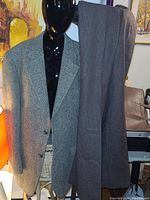 Grey herringbone tweed blazer on mannequin with brown pinstriped dress pants hanging behind.