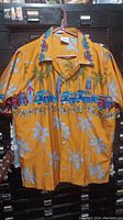 Bright orange Hawaiian shirt with blue vintage wagons, palm trees, and surfboards patterns on a hanger.