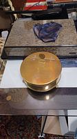Closed brass ashtray beside a mirrored humidor and a folded silk pocket square on a glass surface