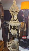 Full view of the macrame table/plant hanger showing its height and multiple sections including the large circular base and hanging midsection with fringe.