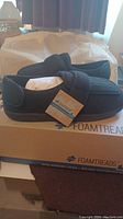 Side view of new FoamTreads shoes on original box showing dark color and general style.