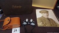 Lot contents showing four vintage black and white military portrait photos alongside the brown leather photo case labeled 'Photographs' and a pair of novelty multi-lens glasses with carrying cord.