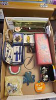 View of assorted pins, brooches, jewelry, and sewing kit in a box