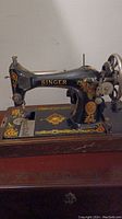 Full side view of the Singer sewing machine showing black body and floral decal design. Machine mounted on a wooden base.