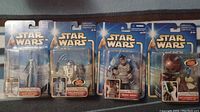 Photo showing four Star Wars collectible action figures in unopened packaging: R2-D2, Dexter Jettster, Yoda with a Force action feature, and a Bounty Hunter/Clone Trooper figure.
