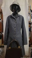 Front view of charcoal gray long wool coat on mannequin with Jane Shilton leather doctors bag visible at bottom, hat on top