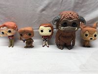 Five Funko Pop figures lined up against white cloth background showing all figures in view.