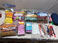 Overall view of boxed and bagged pencils, pens, markers, erasers, and small notebooks on a table.